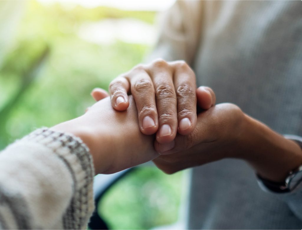 Two hands gently holding each other against a blurred green background.