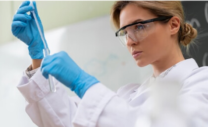 A scientist wearing safety goggles and gloves examines a test tube in a laboratory setting.