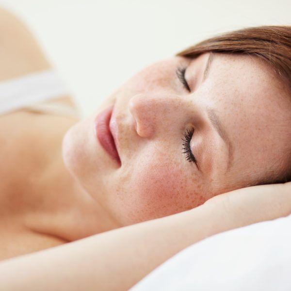 A woman rests peacefully on a white pillow, her head gently supported by her hand, eyes closed in serene relaxation.